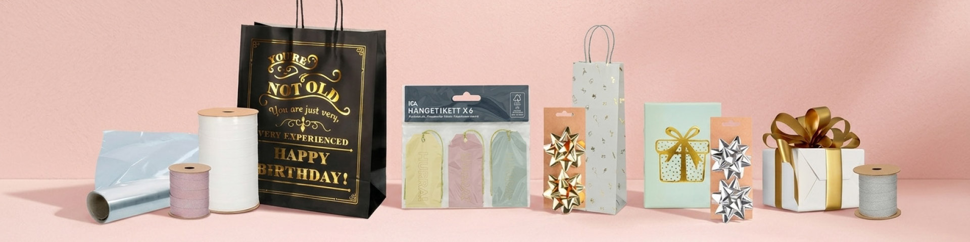 Presentinslagning med presentpåsar, snören, band, etiketter och rosetter. En presentpåse med texten ”YOU’RE NOT OLD YOU ARE JUST VERY EXPERIENCED HAPPY BIRTHDAY!” samt förpackning med texten ”HÄNGETIKETT x6”. Klicka för att handla presentinslagning.