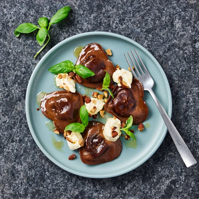 Chokladravioli med apelsinmascarpone, salta mandlar och basilika på en tallrik med en gaffel.