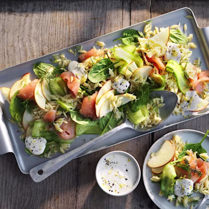 Pastasallad med gravad lax, gurkskivor, äppelskivor, spenat, dill och klickar pepparrotscreme på fat och tallrik.
