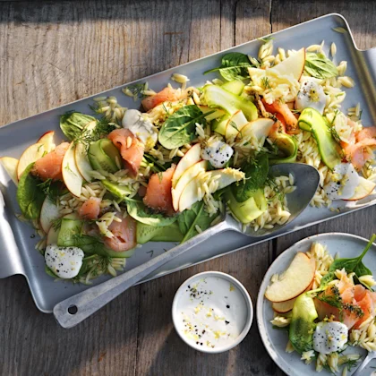 Pastasallad med gravad lax, gurkskivor, äppelskivor, spenat, dill och klickar pepparrotscreme på fat och tallrik.