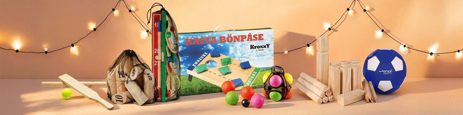 Trädgårdsspel uppställda med kastspel, kubb, bollar och tillbehör samt spelplan, med texten “KASTA BÖNPÅSE Kroxy”. Klicka för att handla.