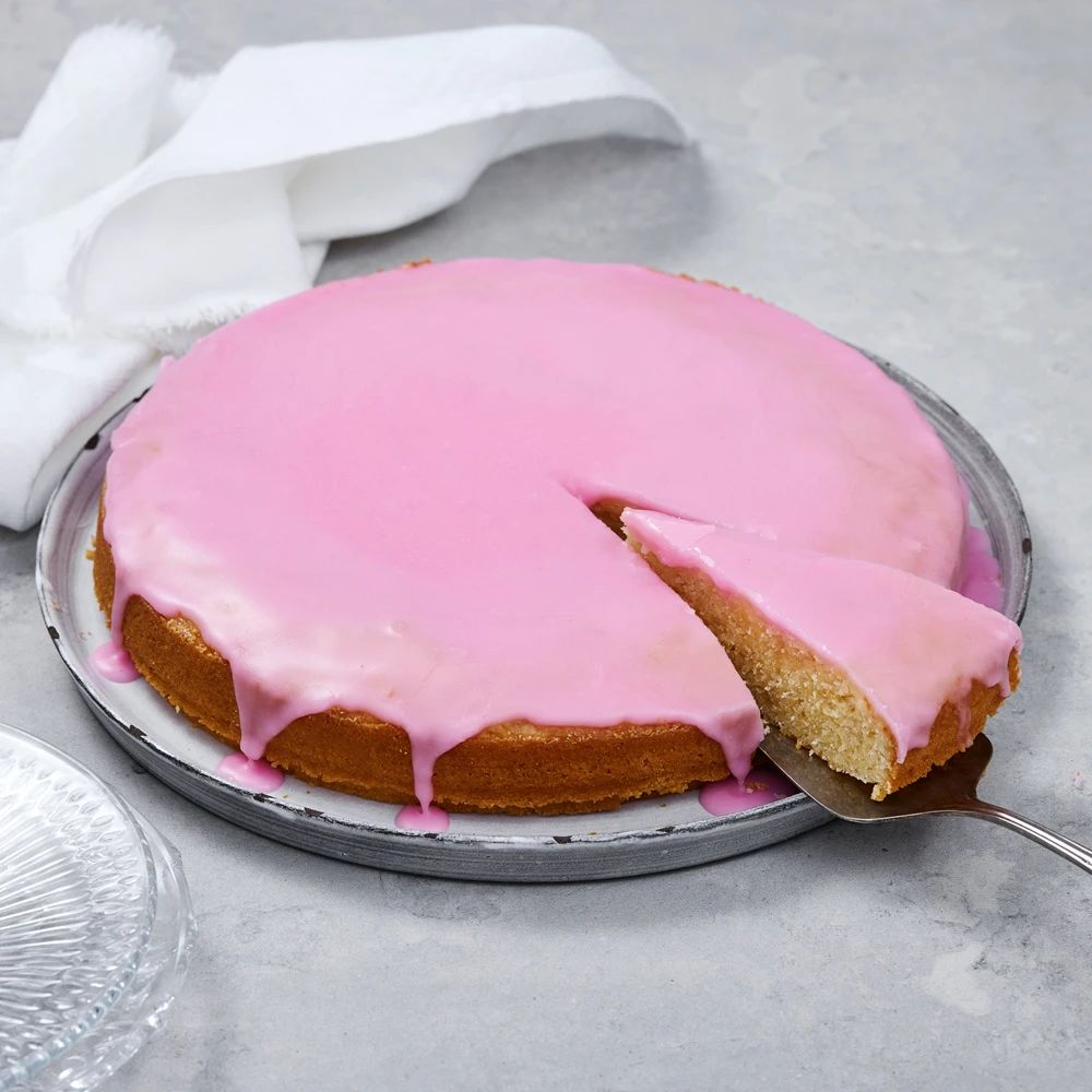 En hel rund stor mazarinkaka med glasyr på ett fat med en bit skuren på en tårtspade