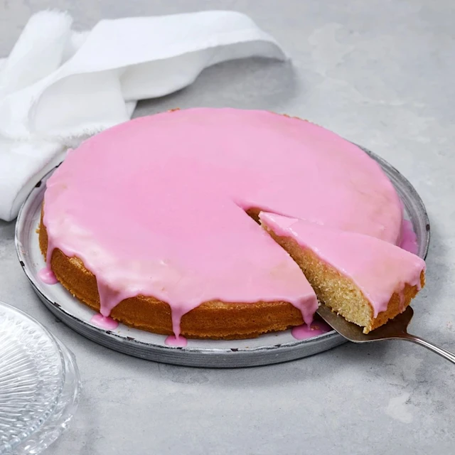 En hel rund stor mazarinkaka med glasyr på ett fat med en bit skuren på en tårtspade