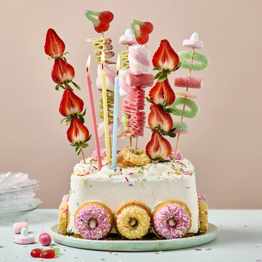 En 2 l glassförpackning på ett fat, kalasdekorerad med små mini donuts, ljus, frukt- och godisspett.