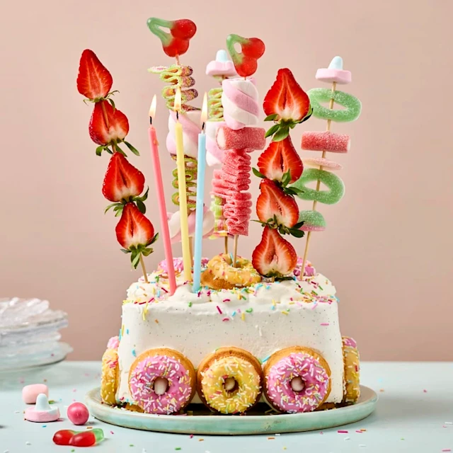 En 2 l glassförpackning på ett fat, kalasdekorerad med små mini donuts, ljus, frukt- och godisspett.