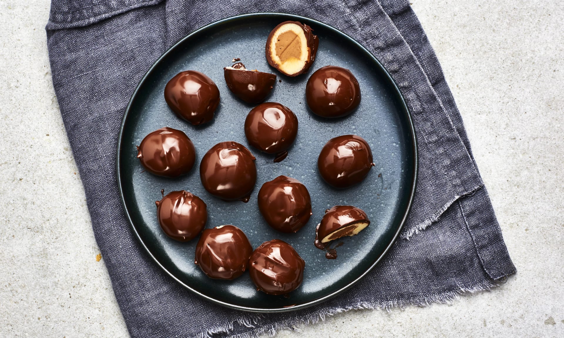 Mozartkulor med chokladöverdrag, några delade så fyllningen syns, upplagda på ett fat.