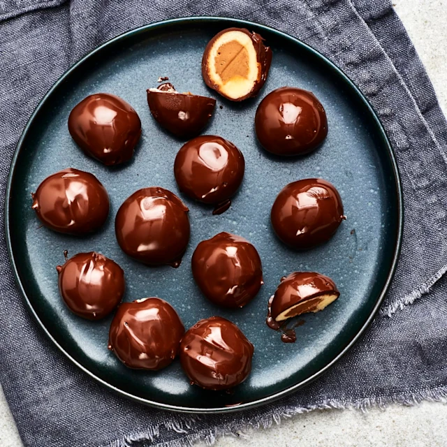 Mozartkulor med chokladöverdrag, några delade så fyllningen syns, upplagda på ett fat.