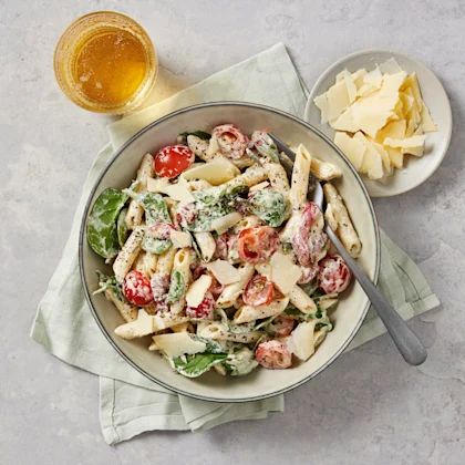 Krämig pastasallad med penne, babyspenat, körsbärstomater och parmesanflarn, serverad i en skål med dryck och extra parmesan bredvid.