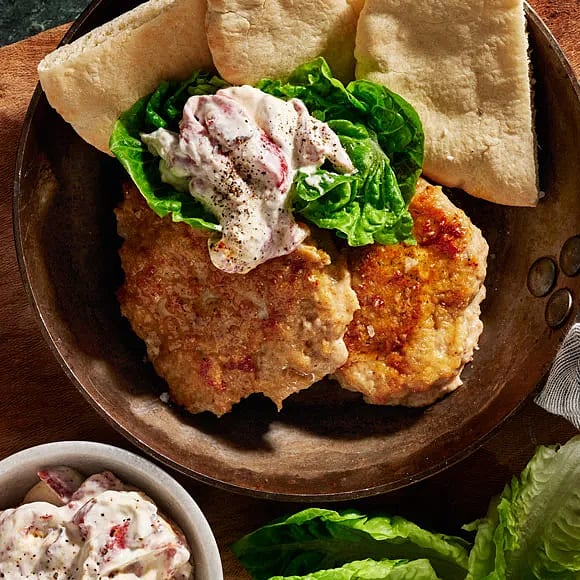 Två bruna köttbullar på en tallrik, med en salladsblad och sås, samt pitabröd i bakgrunden. En skål med sås syns till vänster.