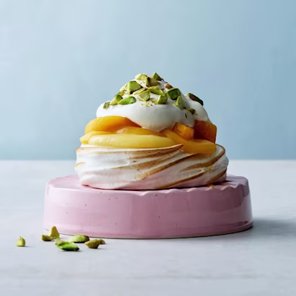 En portionspavlova, maräng med lemoncurd, skivad persika toppad med lättvispad grädde och hackade pistagenötter.