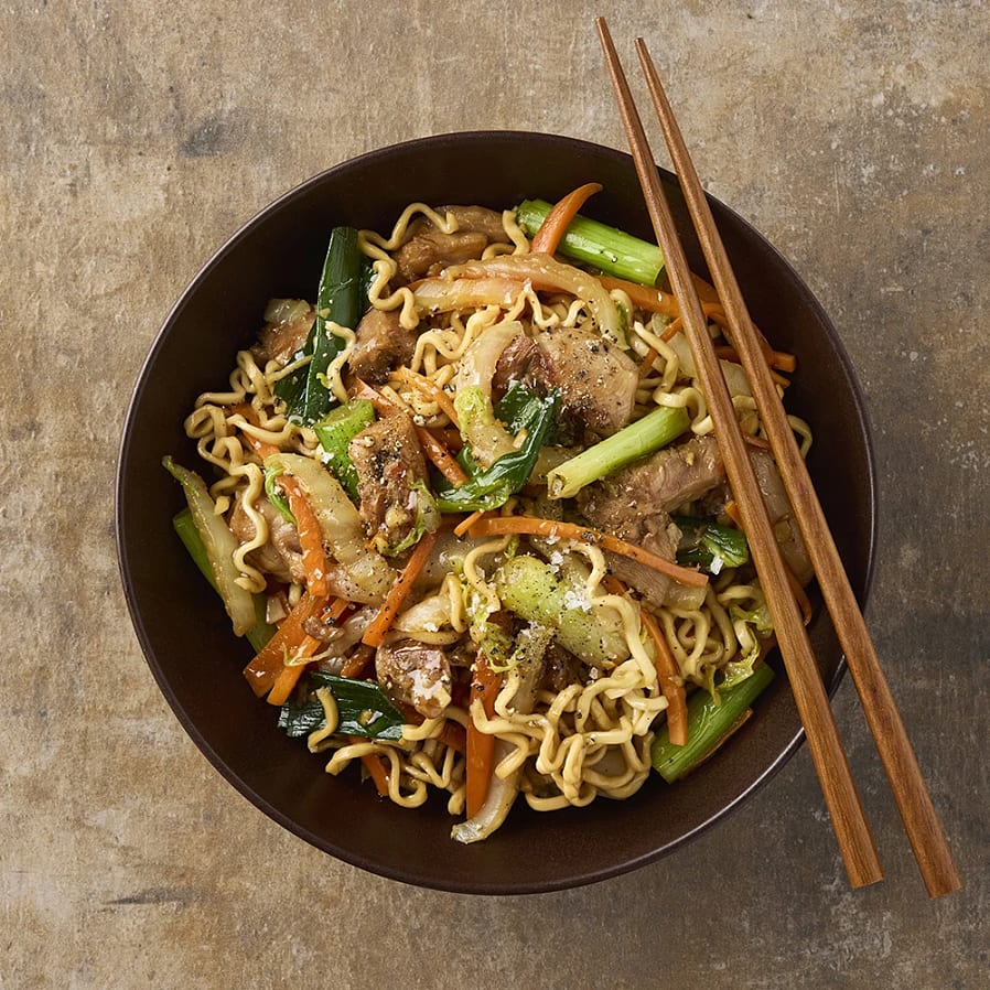 Djup skål med nudlar, strimlad grön lök, morötter och kött. 