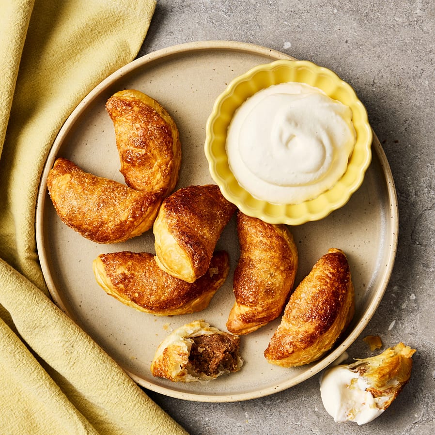 Kanelbulledumplings ligger på ett fat, serverade med en skål vispgrädde som dipp. En dumpling är halverad så fyllningen syns och en bit är doppad i grädden.