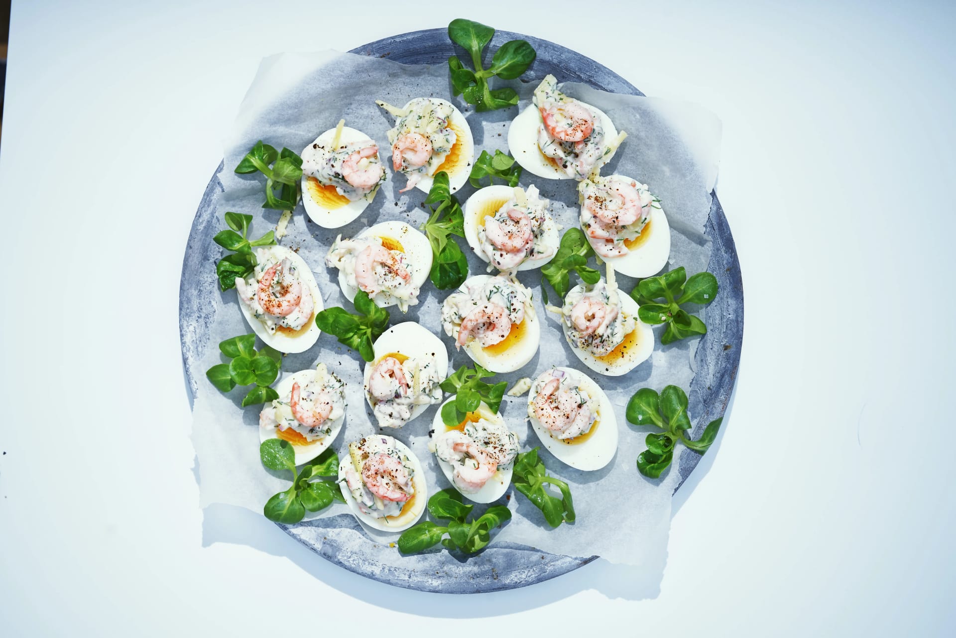 Fyllda ägghalvor ligger på ett fat tillsammans med gröna blad.