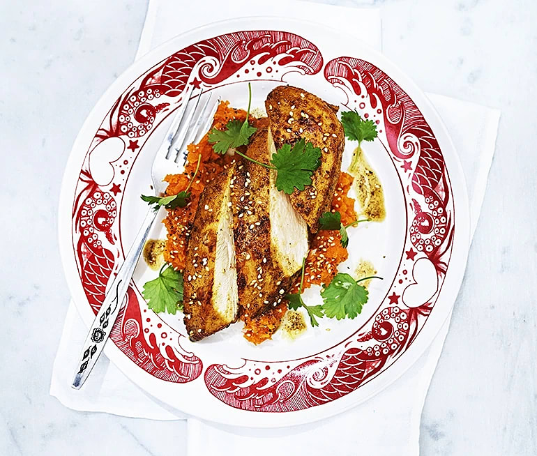 Stekt fiskfilé serverad på en mönstrad tallrik med morotsmos och färsk koriander, garnerad med sesamfrön.