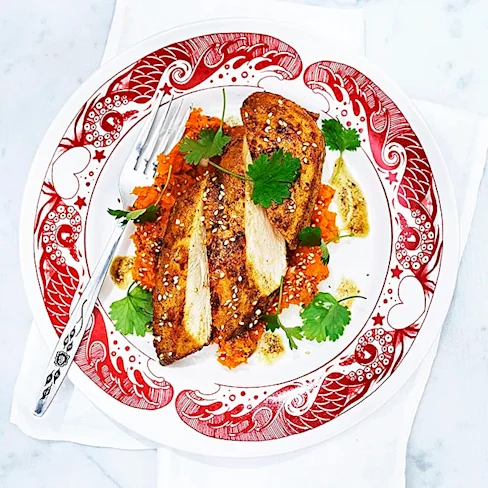 Stekt fiskfilé serverad på en mönstrad tallrik med morotsmos och färsk koriander, garnerad med sesamfrön.