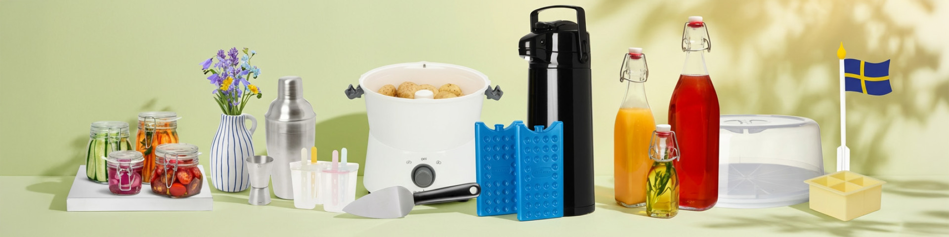 Köksutrustning för midsommar som glasburkar med inläggningar, blommor i vas, shaker, isglassformar, gryta med potatis, termos, kylklampar, dryckesflaskor och tårtfat med svenska flaggor. Klicka för att handla.