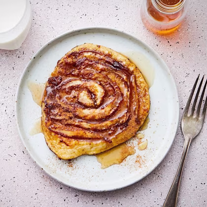Kanelbulle med sirap på en tallrik, serverad med en gaffel och ett glas mjölk i bakgrunden.