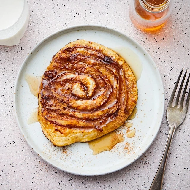 Kanelbulle med sirap på en tallrik, serverad med en gaffel och ett glas mjölk i bakgrunden.