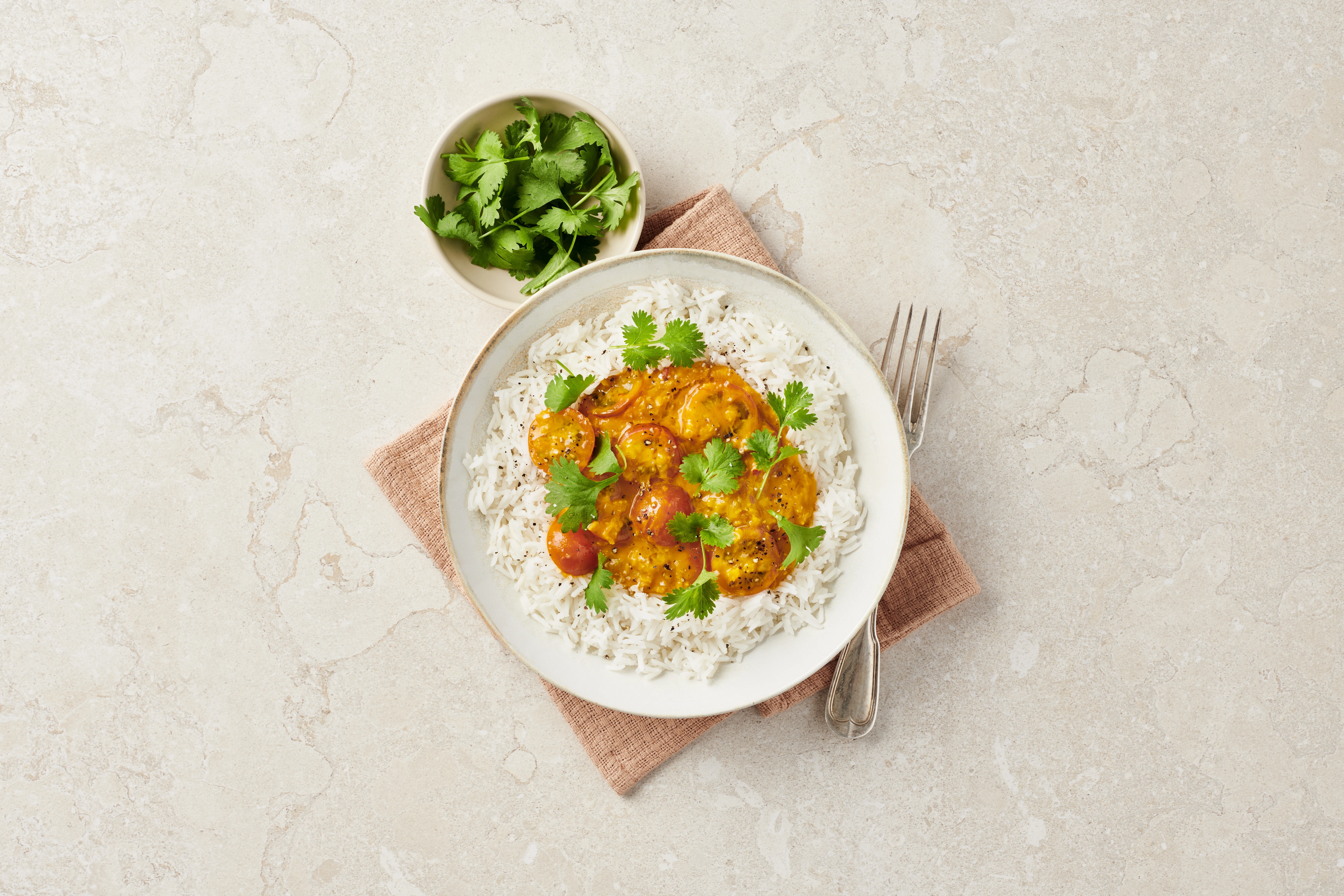 Ris med gryta av räkor i tomat- och currysås, toppat med koriander, serverat med en skål färsk koriander och gaffel.