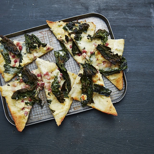 Pizza med svartkål, tärnat bacon och ädelost uppskuret på ett fat