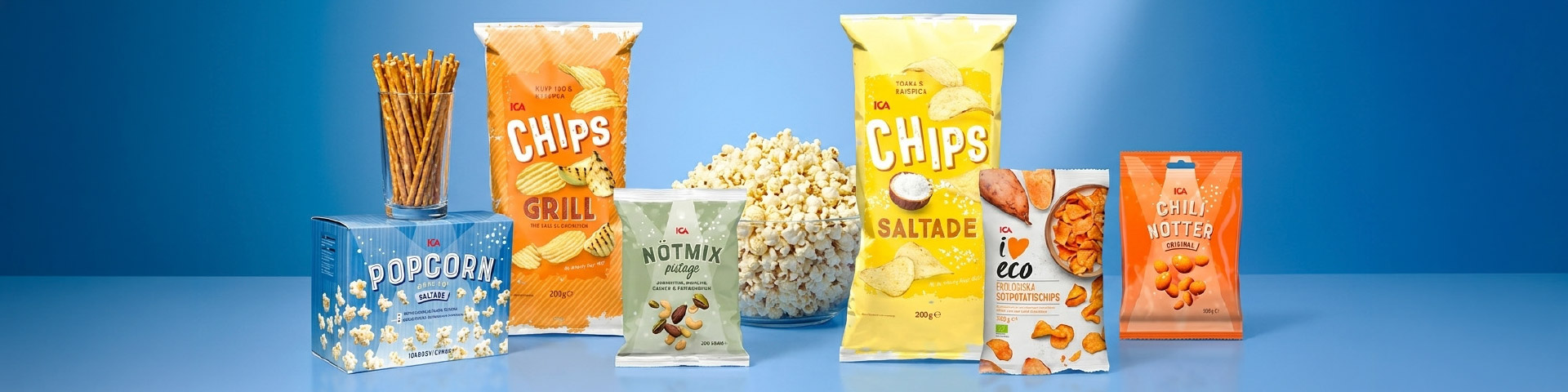 Olika snacksprodukter uppställda, bland annat popcorn, chips grill, saltade chips, nötmix naturell och chili nötter från ICA, med texten “POPcorn”, “Chips Grill”, “Nötmix naturell”, “Chips Saltade Eco” och “Chili nötter”. Klicka för att handla.