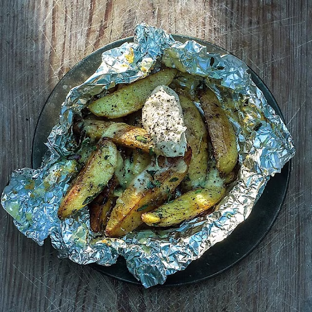 Klyftpotatis i folie med en klick sås och svartpeppar på toppen, serverat på en tallrik.