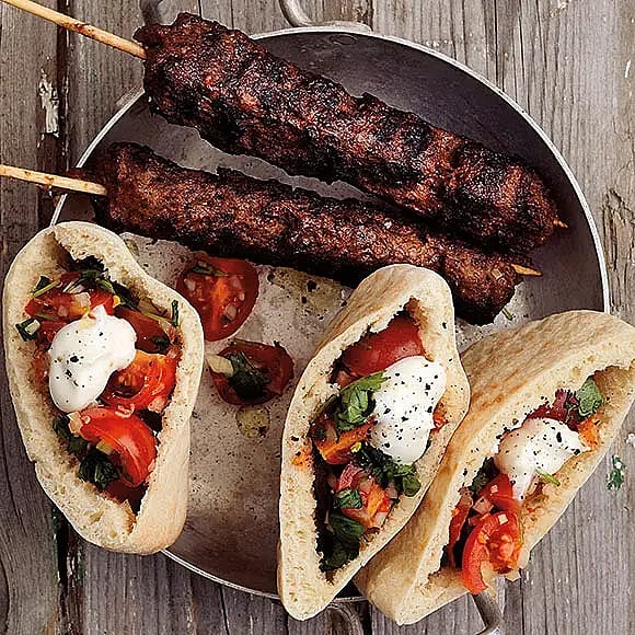 Tre pita med grönsaker och sås, tillsammans med två grillade köttspett, på en metallfat.