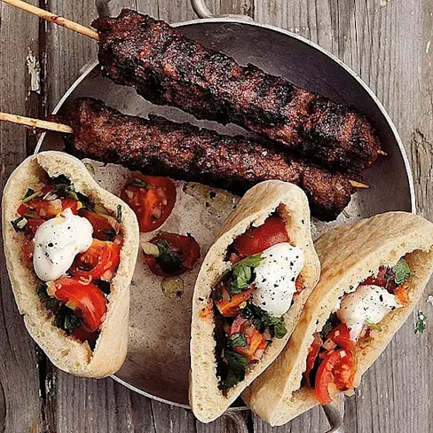 Tre pita med grönsaker och sås, tillsammans med två grillade köttspett, på en metallfat.