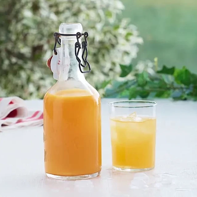 Havtornssaft i en glasfaska med ett glas färdig havtornssaft bredvid.