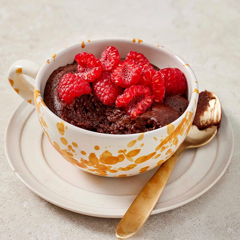 En orangespräcklig tekopp med fat, fylld med kladdkaka och färska bär. 