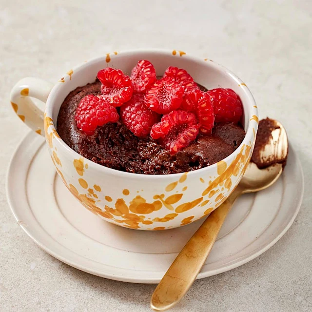 En orangespräcklig tekopp med fat, fylld med kladdkaka och färska bär.