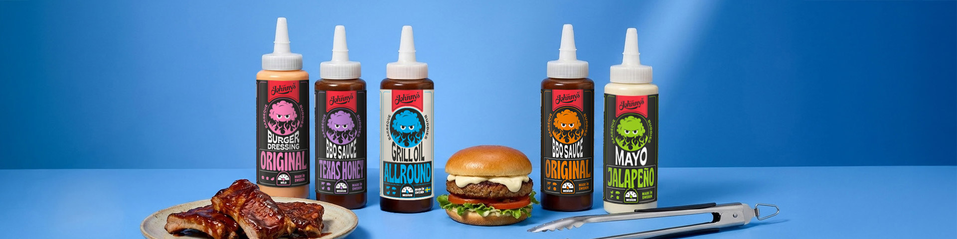 Flaskor med Johnny’s såser: Burger Dressing Original, BBQ Sauce Texas Honey, Grillolja Allround, BBQ Sauce Original och Mayo Jalapeño, tillsammans med hamburgare, revbensspjäll på fat och grilltång. Klicka för att handla.