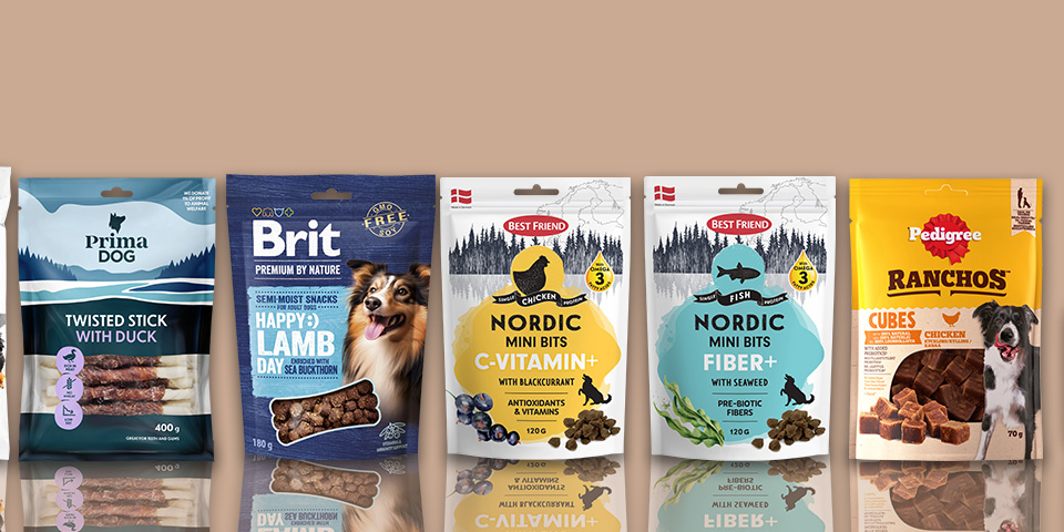 Olika förpackningar med hundgodis och kosttillskott från varumärkena ICA, Prima Dog, Brit, Best Friend, Pedigree och en flaska norsk laxolja står uppradade mot en bakgrund med tassavtryck.