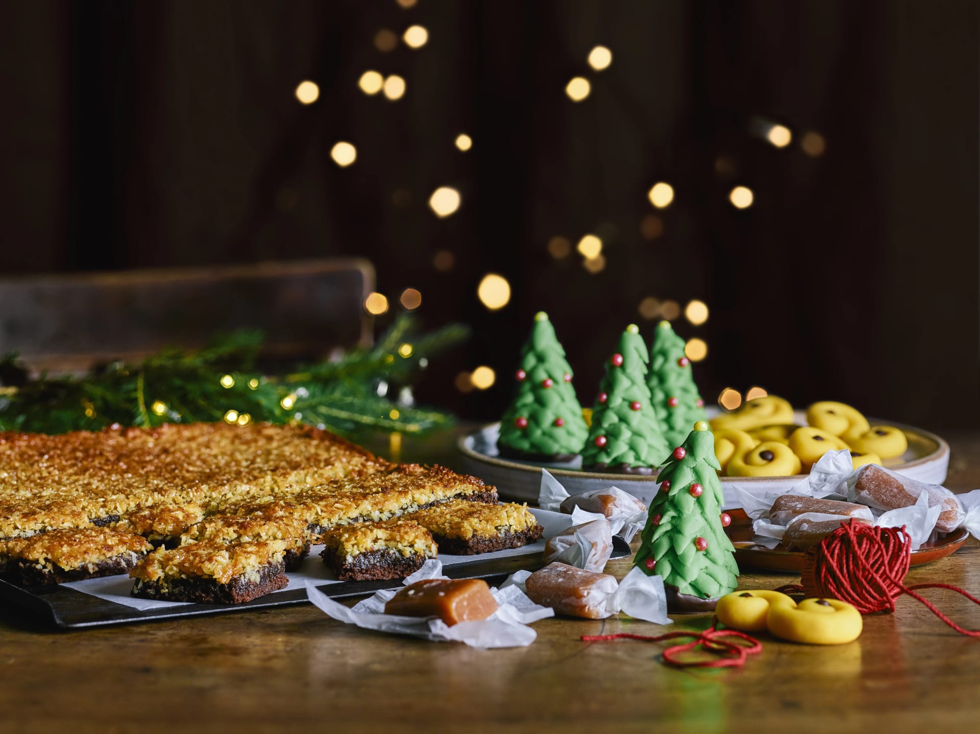 Julbak med saffransbullar, gröna marsipanfigurer formade som julgranar, knäck och bitar av chokladkaka med kokos, upplagt på fat och bricka.