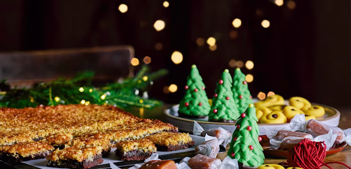 Julbak med saffransbullar, gröna marsipanfigurer formade som julgranar, knäck och bitar av chokladkaka med kokos, upplagt på fat och bricka.