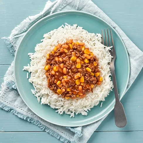 En blå talrik på ett blått bord med ris och en köttgryta med bönor.