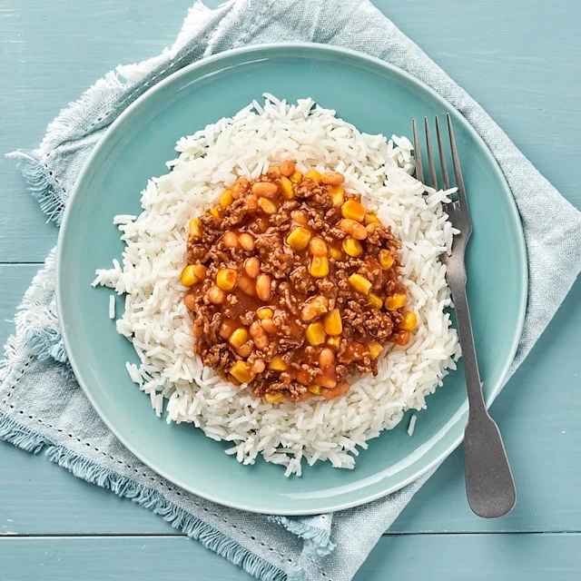 En blå talrik på ett blått bord med ris och en köttgryta med bönor.