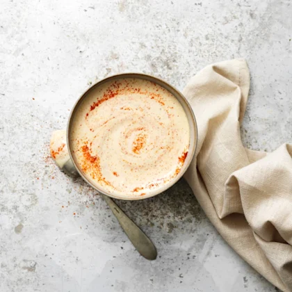 Vit barbecuesås – Alabama white sauce i en skål med paprikapulver som dekoration, en sked ligger till vänster om skålen och en beigeservett ligger till höger om skålen.