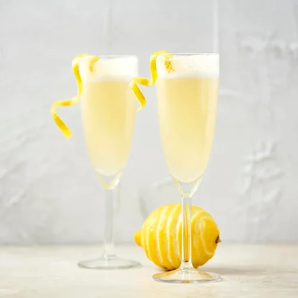 Två champagneglas med skummande citroncocktail och citronskal som dekoration, bredvid en hel citron.