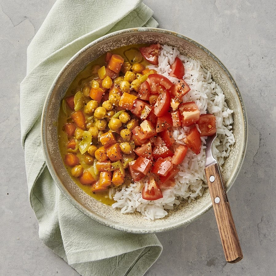 En djup skål med ris, kikärtor, morötter och tomater hackade i småbitar.