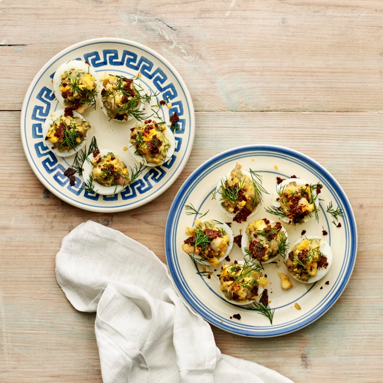 Ägghalvor toppade med matjessill, hovmästarsås, potatis och dill, upplagda på två fat.