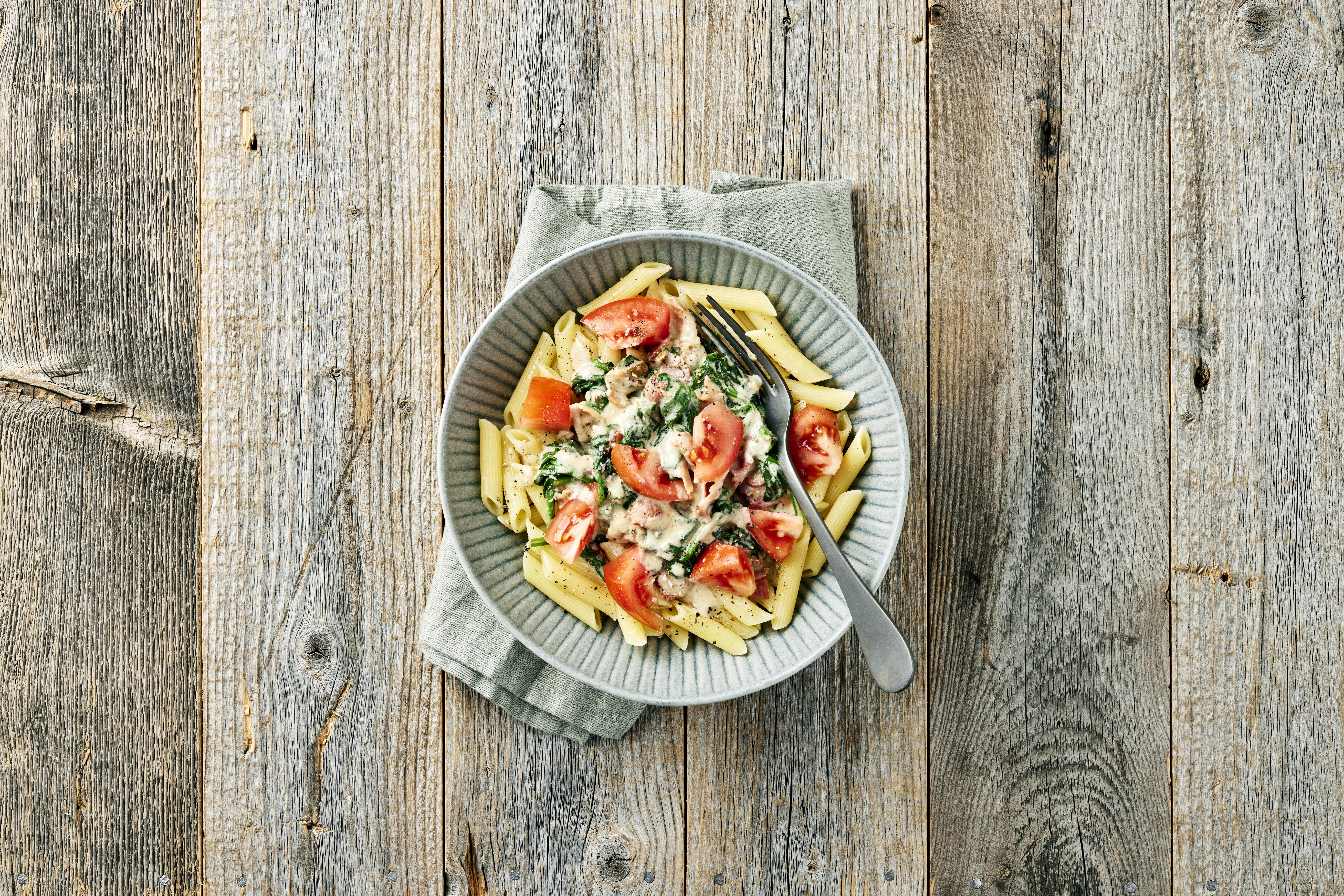 Pasta penne med gräddig sås, spenat och tomatbitar i en skål med gaffel.