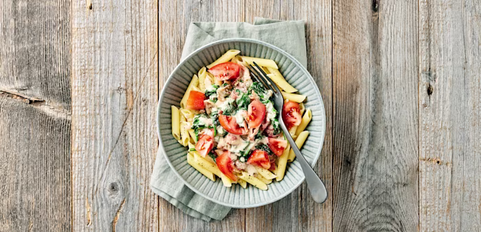 Pasta penne med gräddig sås, spenat och tomatbitar i en skål med gaffel.