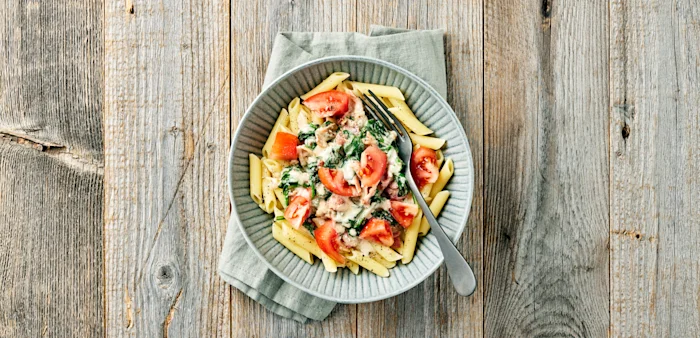 Pasta penne med gräddig sås, spenat och tomatbitar i en skål med gaffel.