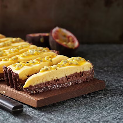 Fryst choklad- och passionstårta skuren i bitar på en skärbräda, toppad med passionsfrukt, med en kniv och en halverad passionsfrukt bredvid.