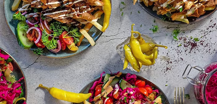 Tre tallrikar med kebab, pommes frites, grönsaker och sås, omgivna av picklade grönsaker och chilifrukter.
