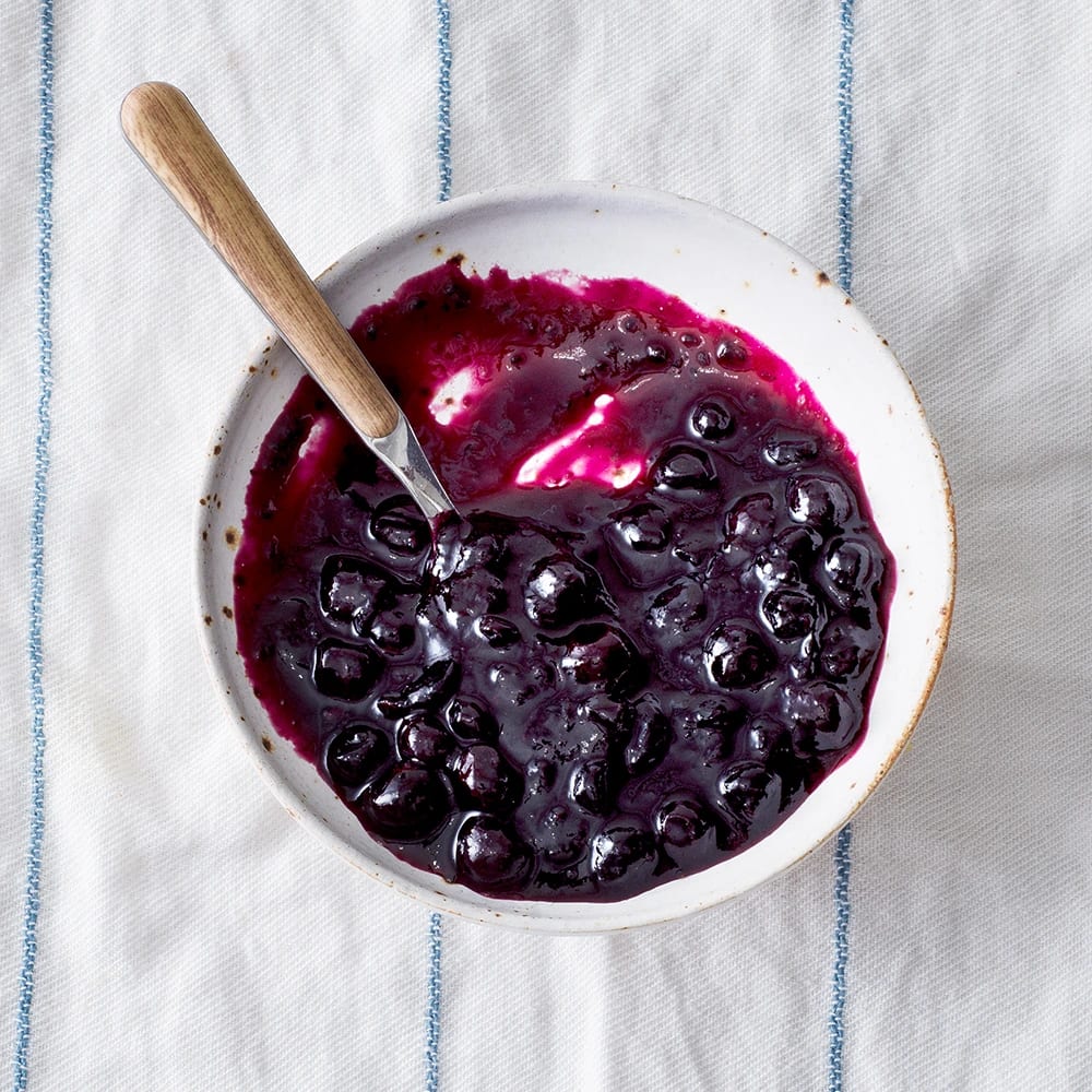 Svartvinbärssylt med kardemumma i en skål, med en sked som vilar på kanten.