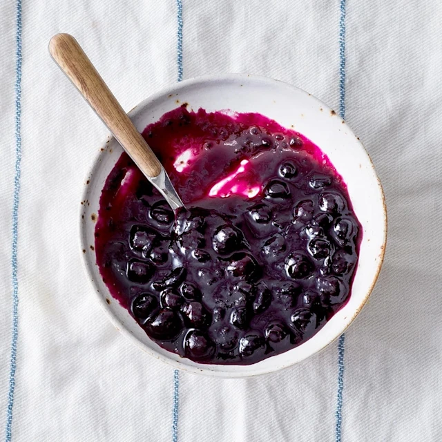 Svartvinbärssylt med kardemumma i en skål, med en sked som vilar på kanten.
