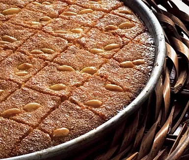 Söt bakelse med fyrkantiga bitar och mandlar på toppen, serverad i en rund form.