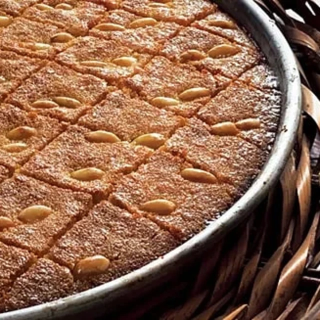 Söt bakelse med fyrkantiga bitar och mandlar på toppen, serverad i en rund form.